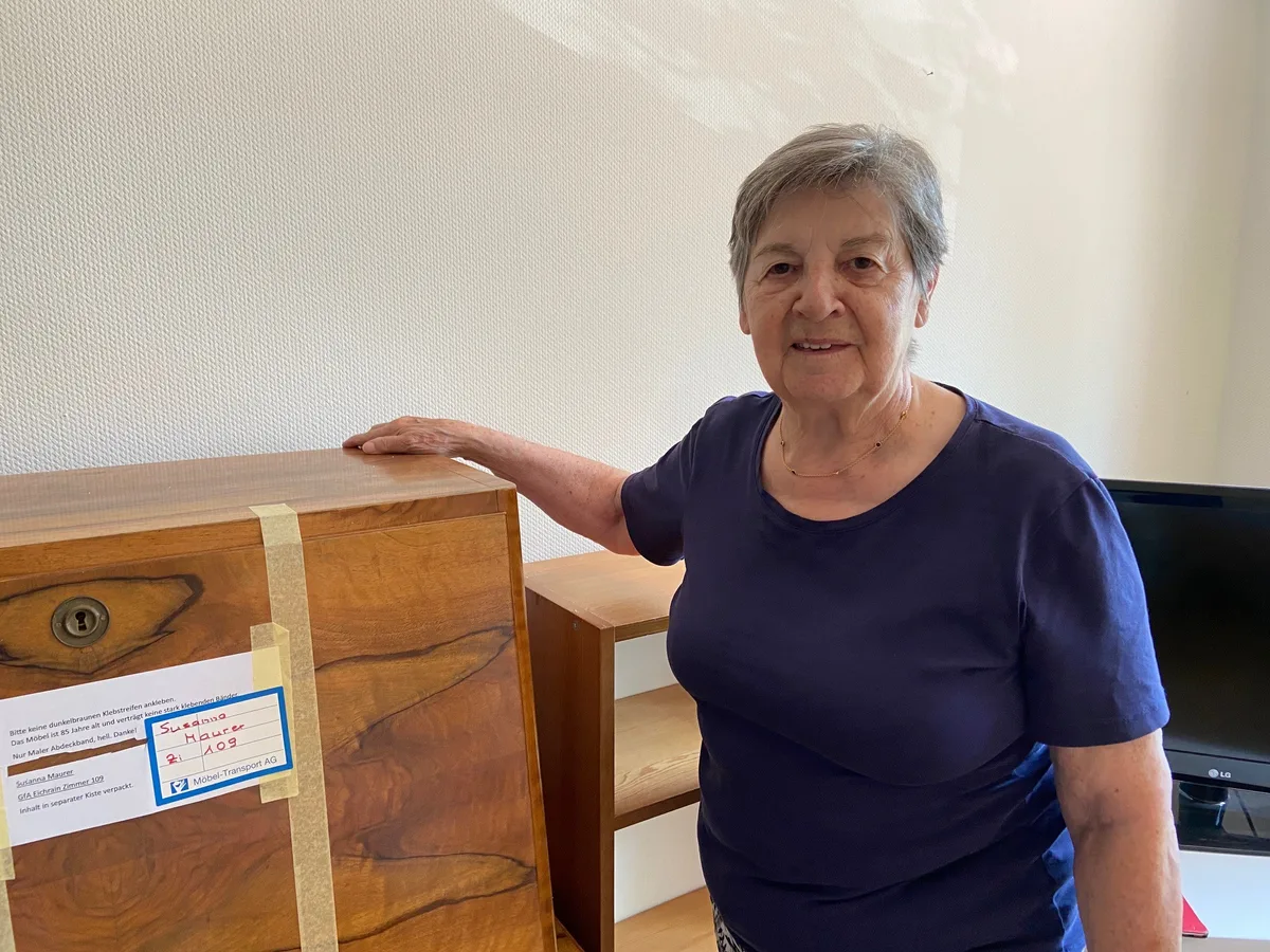 Susanna Maurer neben einem Sekretär aus Holz.